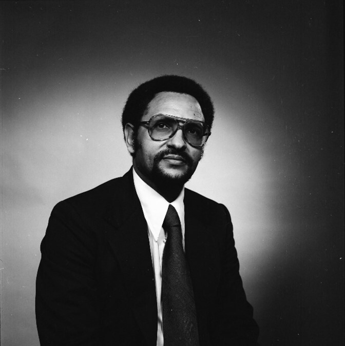 Photograph of Dr. Admaso Zike sitting down and wearing a suit, tie and glasses. 