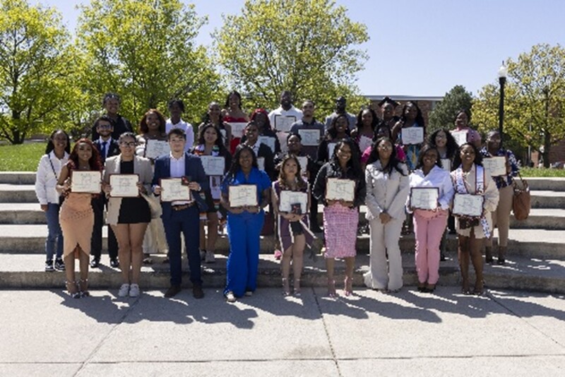 Photo of a couple dozen NIU students who are part of the CHANCE program standing outside on stairs dressed up and holding a certificate to celebrate graduation. 