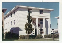 Historic photo of Kappa Alpha Psy Fraternity Inc. House. It's a white three-story building with 2 pillars on the front and the Greek letters in red on the front. 